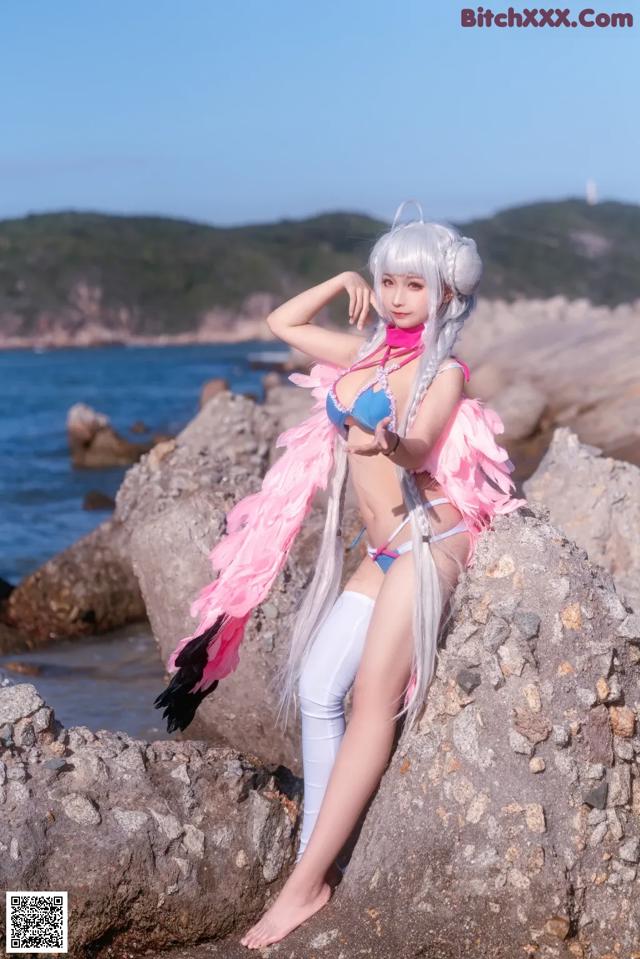 A woman in a bikini sitting on a rock by the ocean.