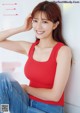 A woman in a red tank top sitting on the ground.