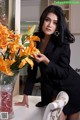 A woman in a black suit sitting at a table with a vase of flowers.