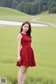 A woman in a red dress standing in a green field.