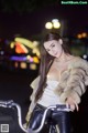 A woman in a fur coat riding a bike at night.