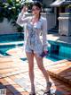 A woman standing next to a swimming pool wearing a white shirt and shorts.