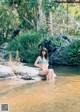 A woman in a blue bikini sitting on a rock in the water.