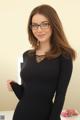 A woman in a black dress and glasses posing for the camera.