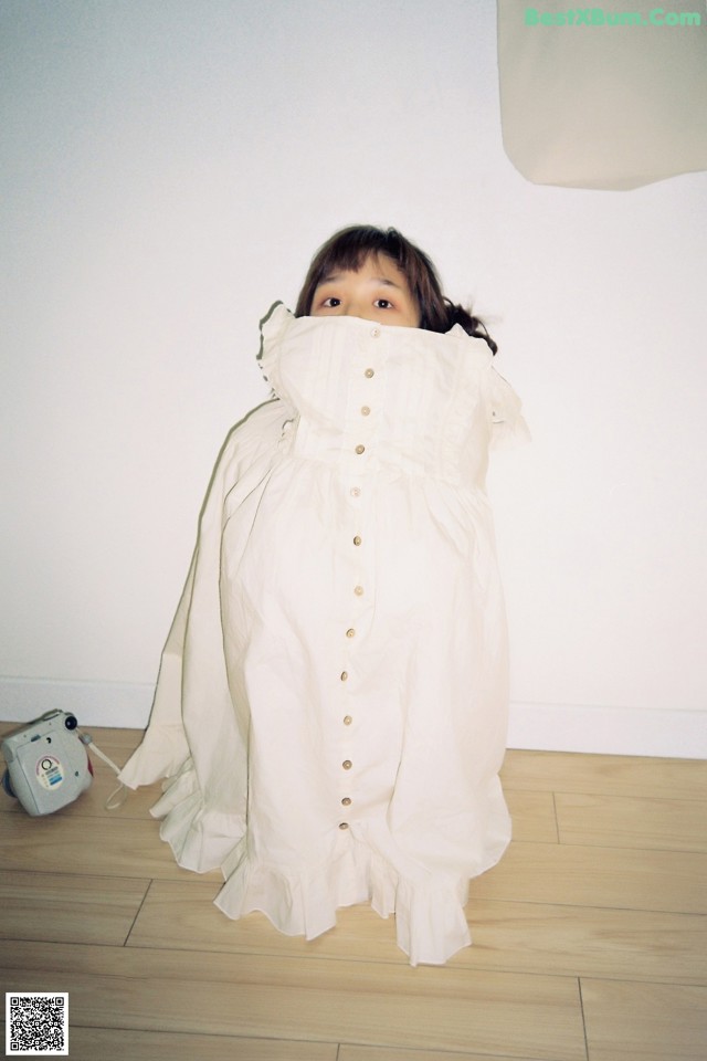 A little girl in a white dress standing on a wooden floor.