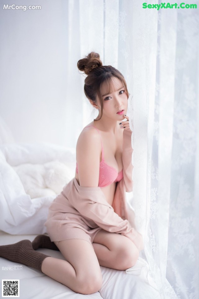 A woman in a pink lingerie sitting on a bed.