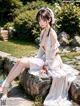 A woman in a white dress sitting on a rock by a pond.