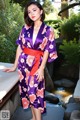 A woman wearing a purple and orange kimono standing next to a pond.